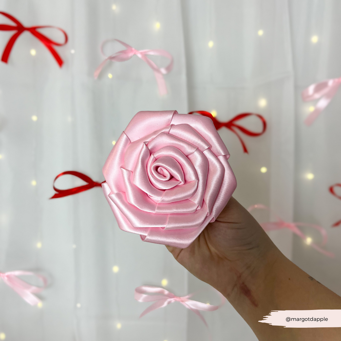Hand holding Cocopup London Pink Rose Collar Flower; pink velvet dog corsage and ribbon bows with fairy lights in background.