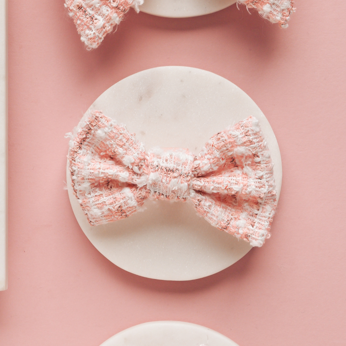 Pink textured tweed bow tie by Cocopup London, shown on a white surface with a pastel pink background.