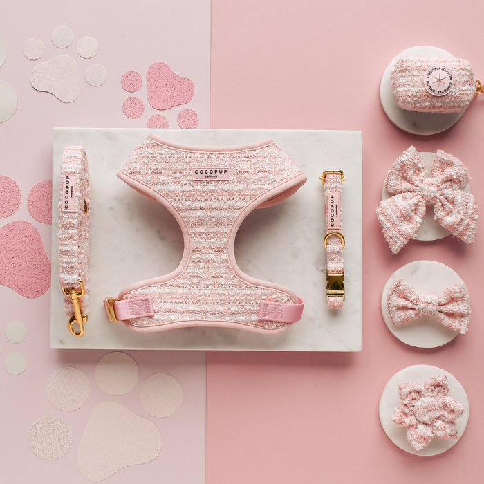Pink textured tweed dog collar with flower, matching leash, bowties, and waste bag holder on a pink marble surface.