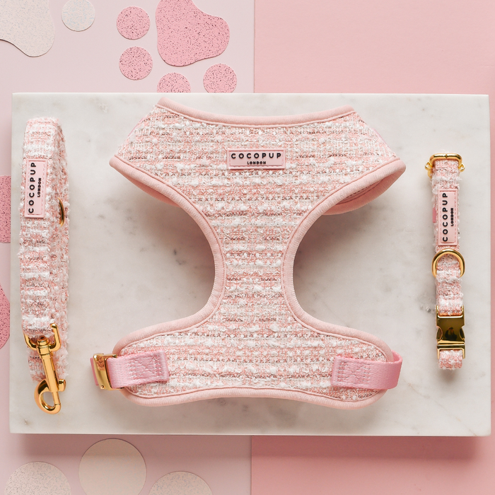 Pink tweed adjustable harness, lead, and collar set with gold hardware on a marble pink background with paw prints.