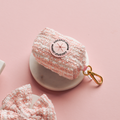 Pink textured tweed poop bag holder with gold clip on a white dish beside a matching accessory.