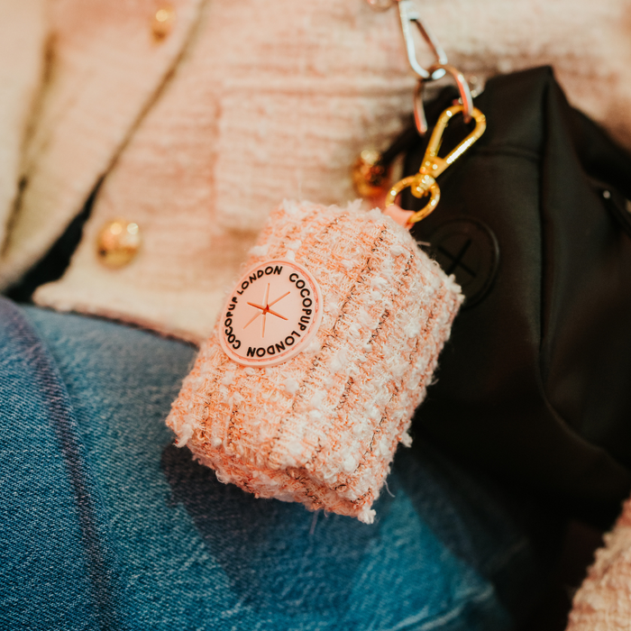 Pink textured tweed poop bag holder by Cocopup London clipped to a black bag, blue jeans visible in background.