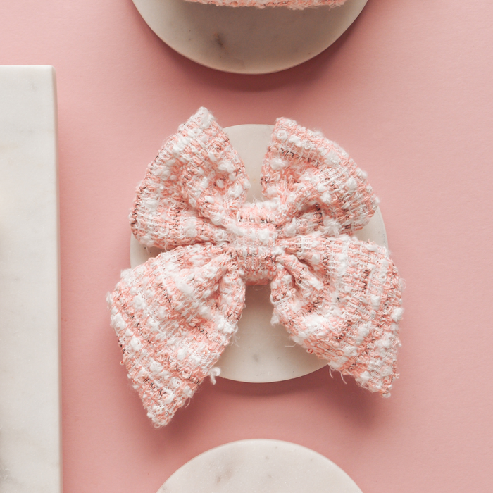 Pink textured tweed sailor bow tie by Cocopup London on a round white surface, set against a pink background.