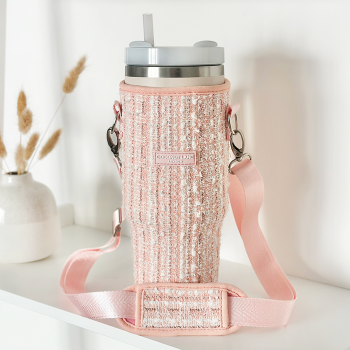 Pink textured tweed tumbler carry case with handle on a white shelf next to dried beige flowers.