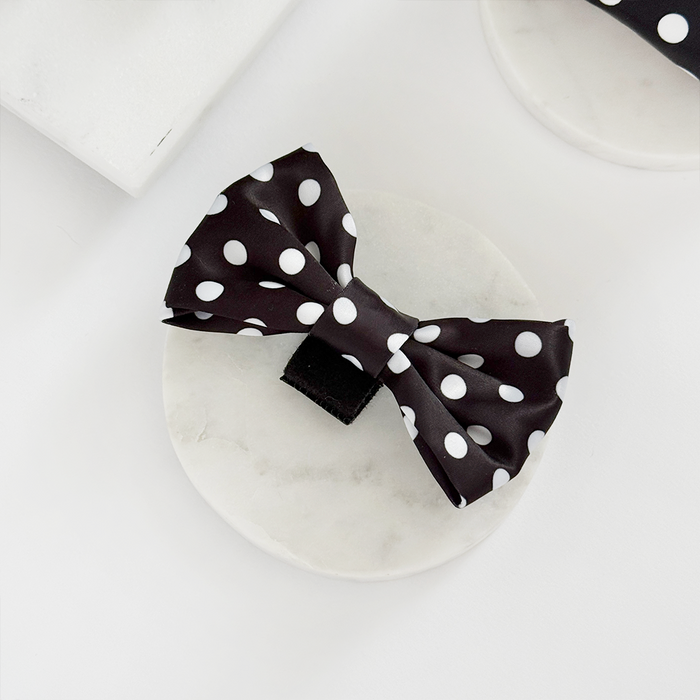 Cocopup London polka dot bow tie with black spots on white fabric, set on a round white marble surface.