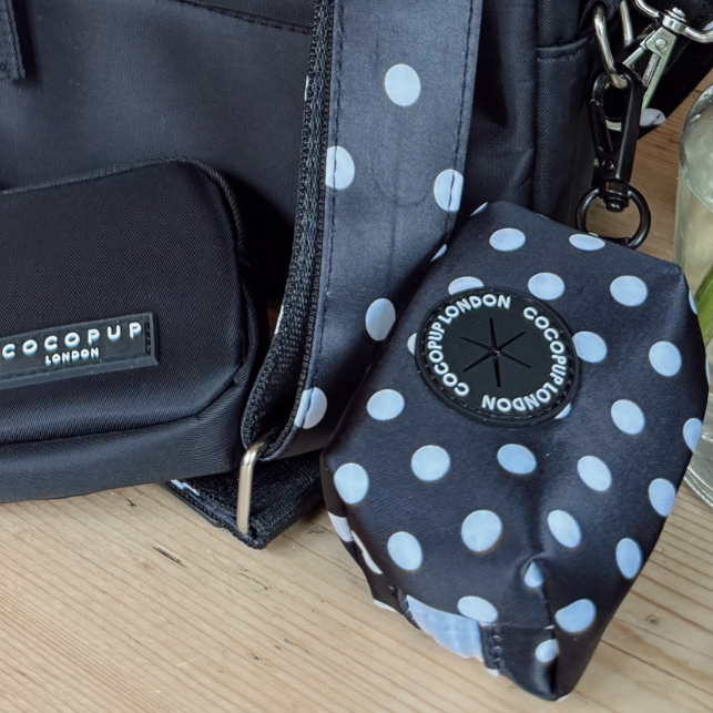Black bag and Cocopup London polka dot poop bag holder on a wooden surface.