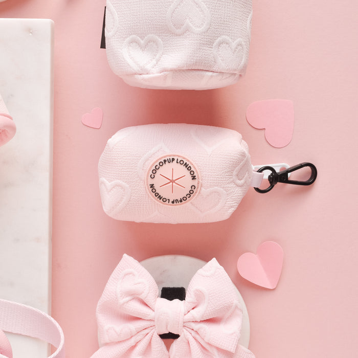Baby pink heart-patterned poop bag holder with gold-tone carabiner, compact and stylish design.