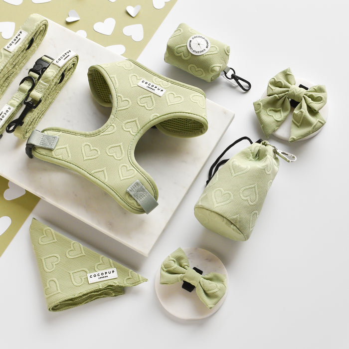 Sage green heart-patterned Cocopup London Luxe poop bag holder with matching dog accessories on a marble surface.