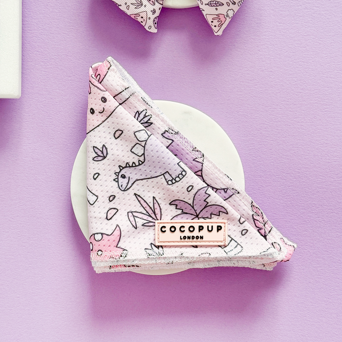 Pink Cocopup London bandana with dinosaur print, folded on a white surface with a purple background.