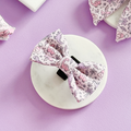 Princess Dino Bow Tie by Cocopup London, pastel dinosaur pattern, displayed on a white platform with lavender background.