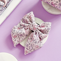 Princess Dino Sailor Bow Tie with pastel dinosaur print by Cocopup London displayed on a dish against a purple background.