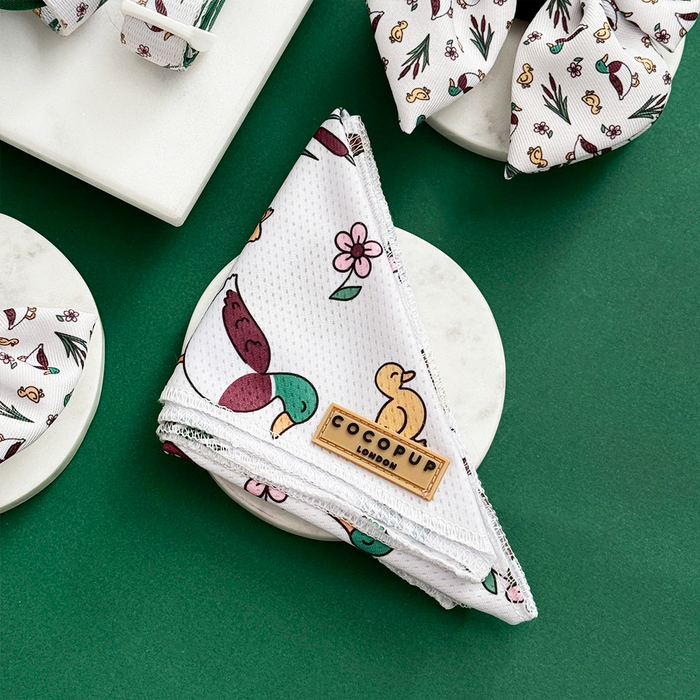 Folded dog bandana with duck and flower print, by Cocopup London, shown on a green background.