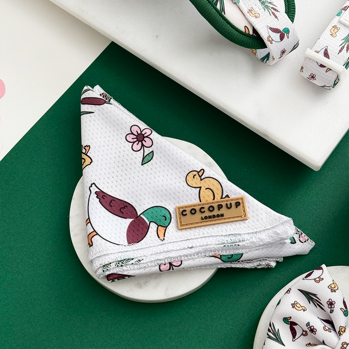 White Cocopup London bandana with duck and floral print, folded on marble surface, green background.