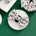 Puddle Pup Bow Tie by Cocopup London with a mushroom and leaf print, displayed on a round marble surface.