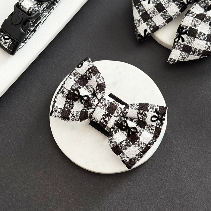 Black and white check bow tie with paw prints by Cocopup London on a white round surface.