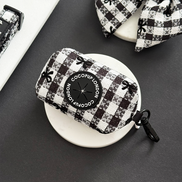 Black and white plaid Cocopup London Pup in Paris poop bag holder on a white circular surface.