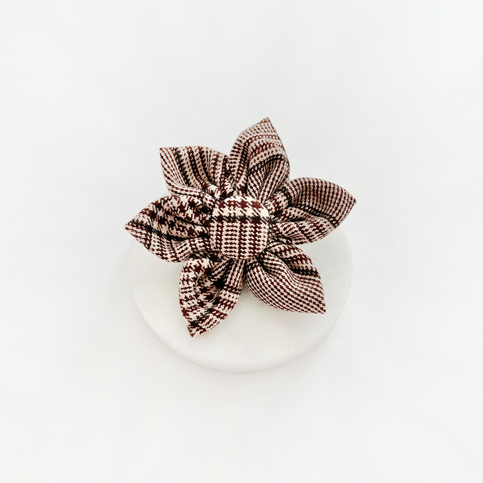 Brown and white plaid dog collar flower with pointed petals on a round white surface.
