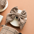 Brown and beige plaid Cocopup London Pup Sailor Bow Tie displayed on a white dish against a tan background.