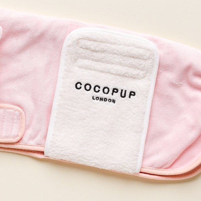 The PRE-ORDER Pupicorn Drying Robe from Cocopup London is crafted from an elegant Premium Microfibre material in a soft pink shade. It features a white patch emblazoned with "Cocopup London" in black text. This luxurious robe, laid flat on a light surface, appears to have velcro straps for easy adjustment.