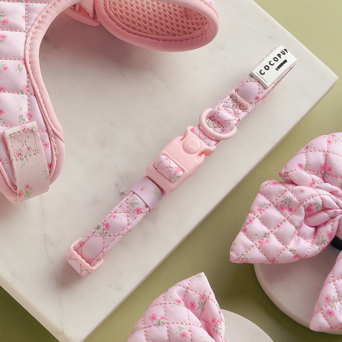 Pink quilted floral harness, lead, and collar set on a marble and green background.