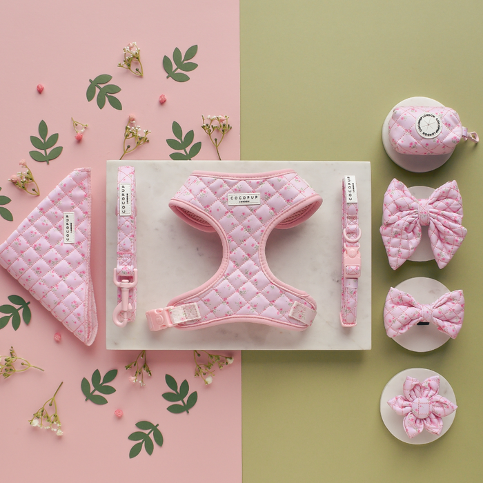 Pink quilted dog bow tie with ditsy floral pattern, displayed on a pink and green background.