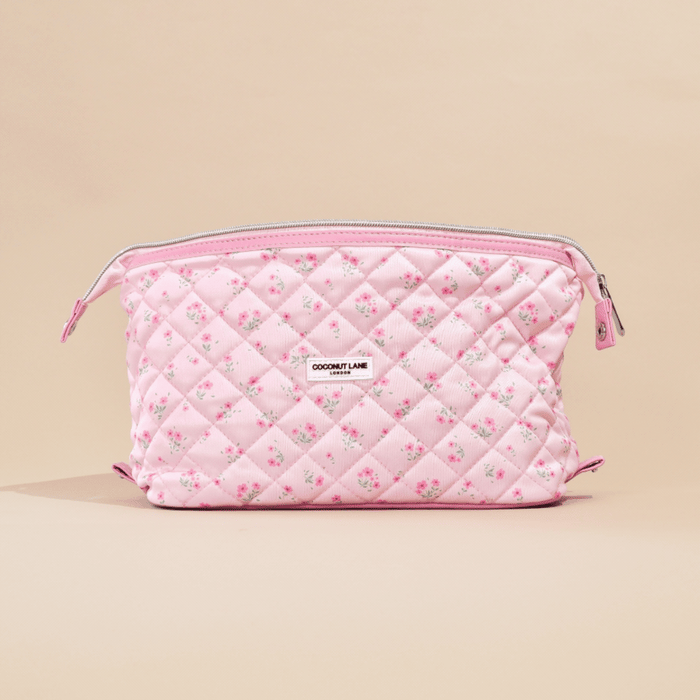 Quilted pink makeup bag with ditsy floral print and expandable design, shown on a beige background.