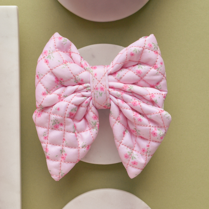 Quilted pink sailor bow tie with a ditsy floral pattern from Cocopup London, displayed on a pale round surface.
