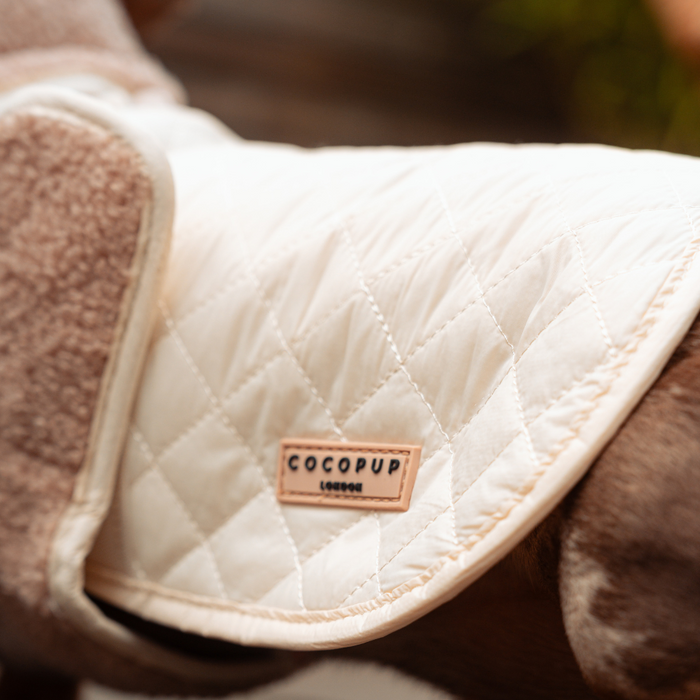Cream quilted dog coat with stitched pattern and a small brown branded leather tag.