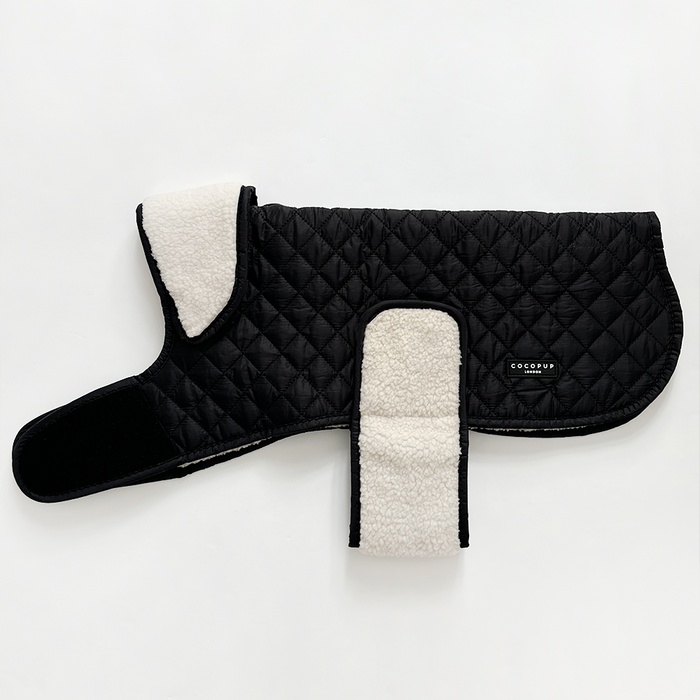 Midnight black quilted dog coat with white fleece lining, Velcro straps, and a side logo tag.