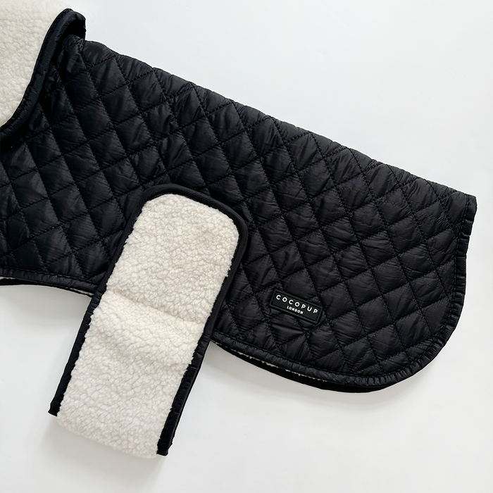 Black quilted Cocopup dog coat with white teddy fleece lining and a Velcro strap.
