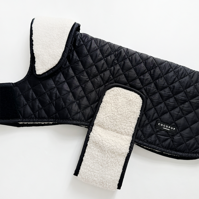 Black quilted dog coat with white teddy lining, shown on a plain white background.