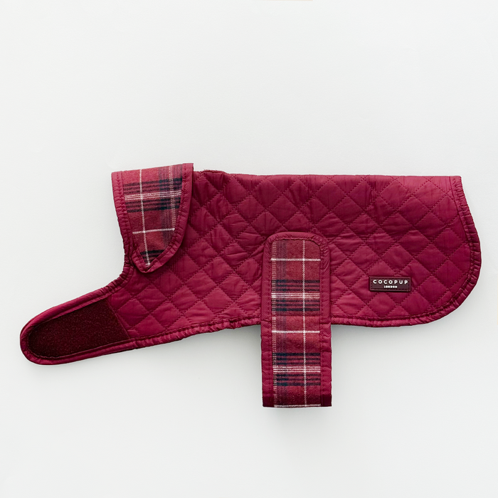 Quilted dog coat in mulberry plaid with Velcro straps, laid flat on a white background.