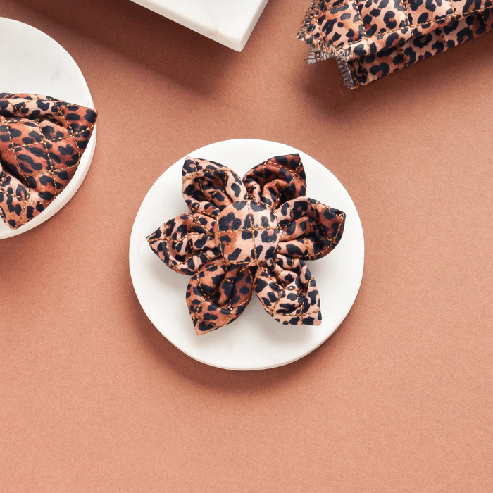 Quilted leopard print dog collar flower by Cocopup London on a white marble and brown background.