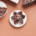Quilted leopard print dog collar flower by Cocopup London on a white marble and brown background.