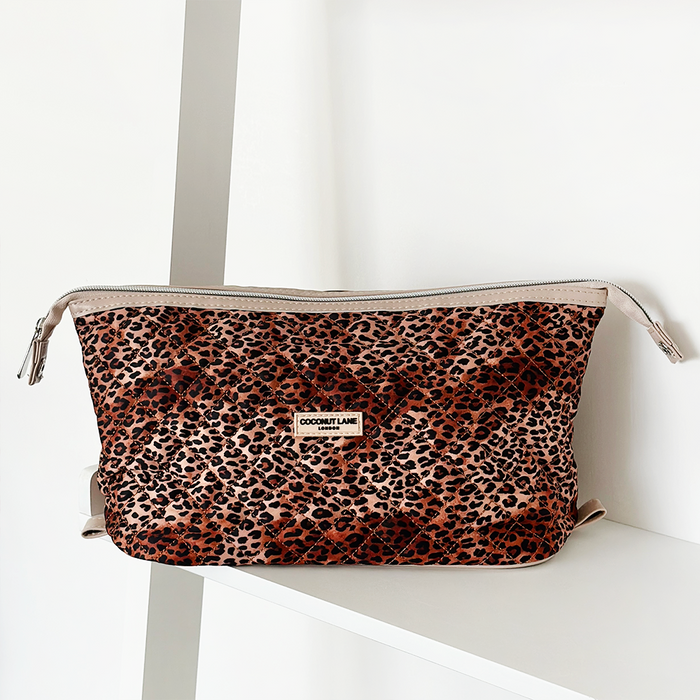 Quilted expandable makeup bag with a leopard print, displayed on a white shelf.