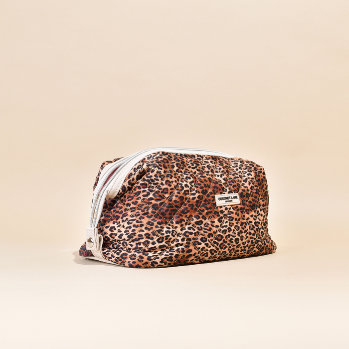 Expandable quilted makeup bag with leopard print, white label, shown on a neutral beige background.