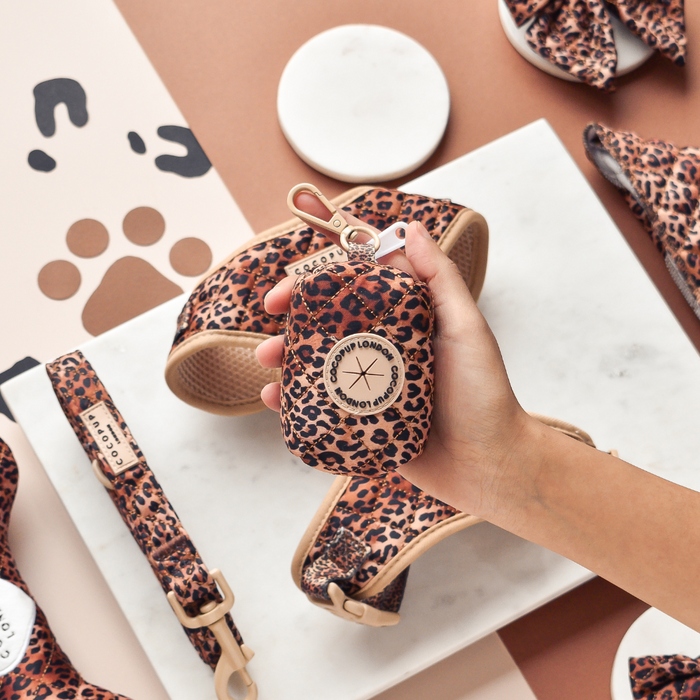 Quilted leopard print poop bag holder and matching accessories held in a hand on a marble surface.