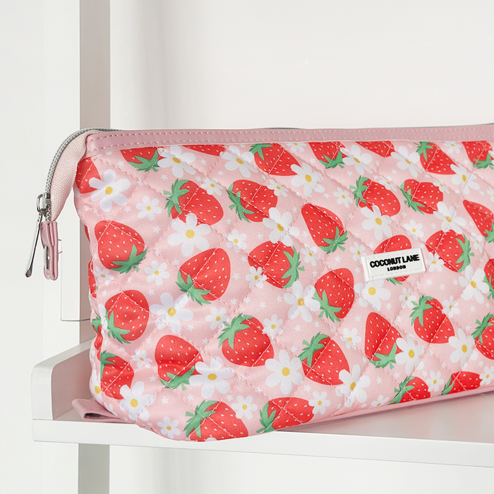 Quilted expandable makeup bag with strawberry and daisy print, displayed on a white shelf.