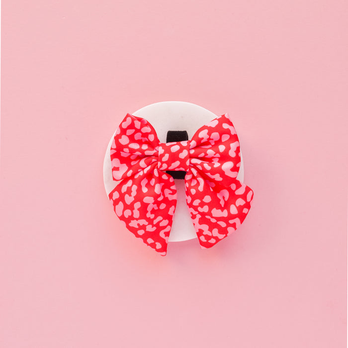 Red and pink leopard print sailor bow tie on a round white display, set against a pink background.