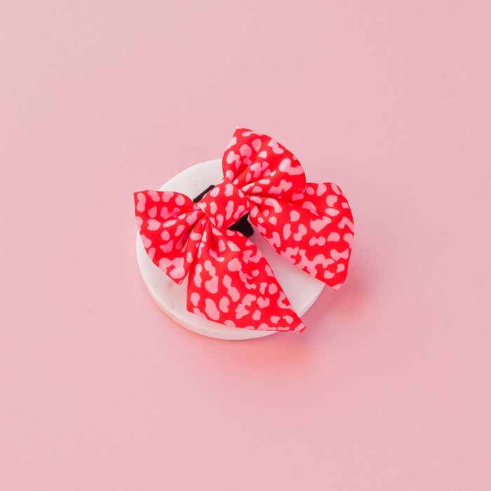 Red and pink leopard print sailor bow tie on a round base, set against a pink background.