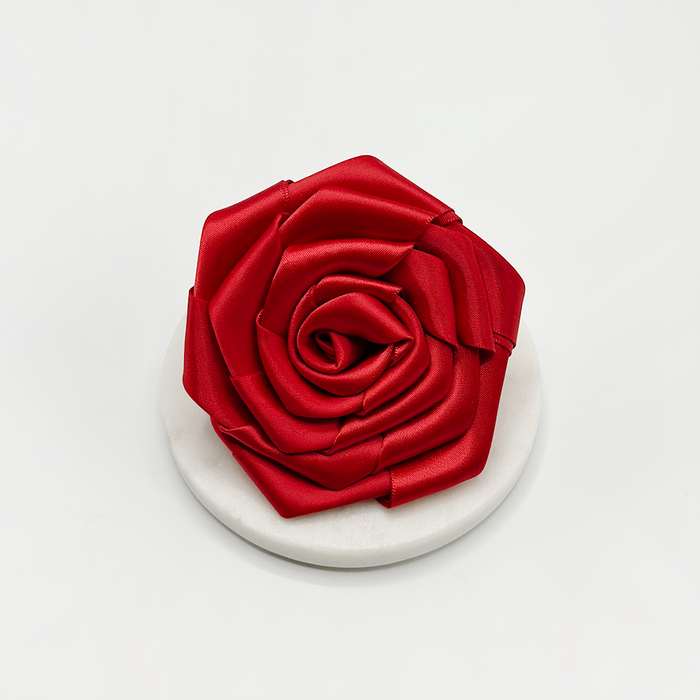 Red rose-shaped dog collar flower by Cocopup London on a white marble coaster, set against a plain white background.