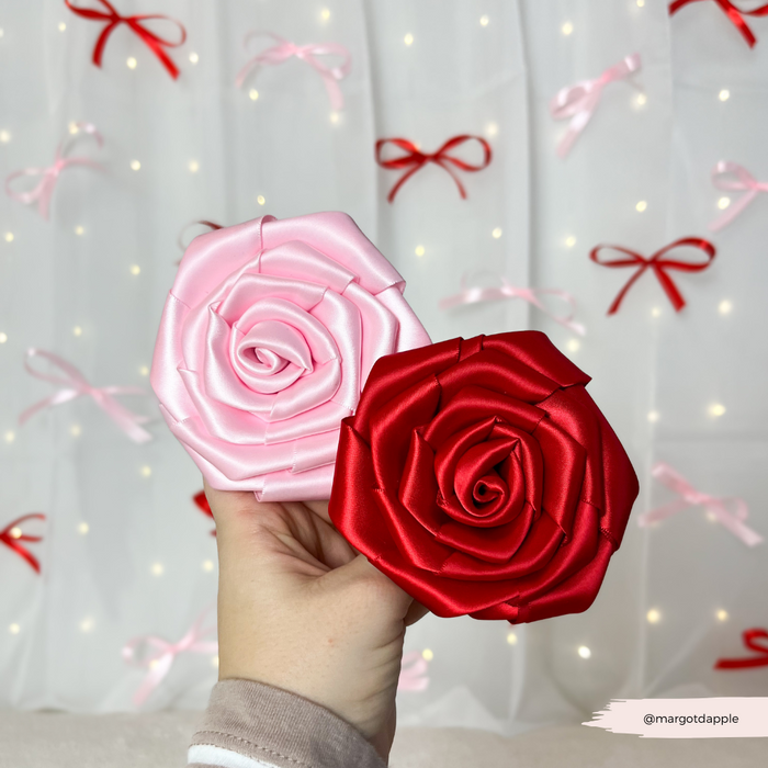Hand holding Cocopup London Red Rose Collar Flower with pink and white fabric; string lights softly blurred behind.