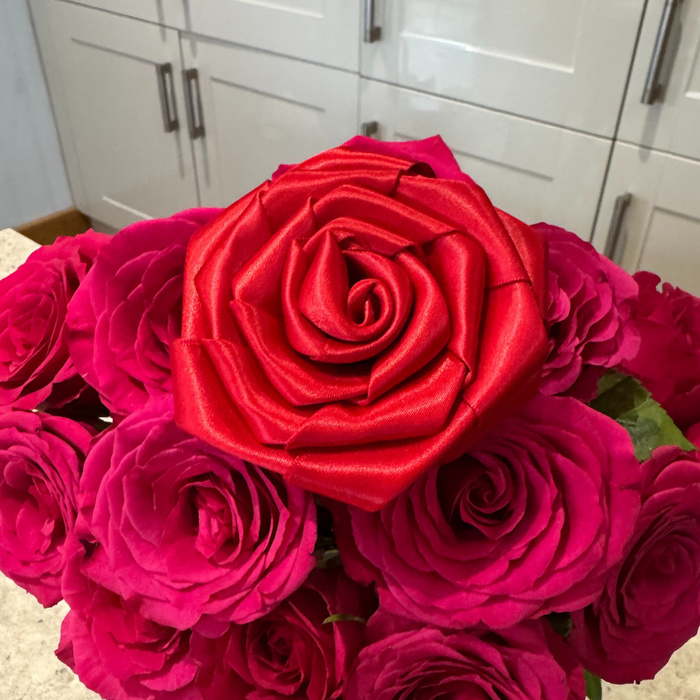 Red Cocopup London rose collar flower displayed on pink roses, shown on a kitchen counter.