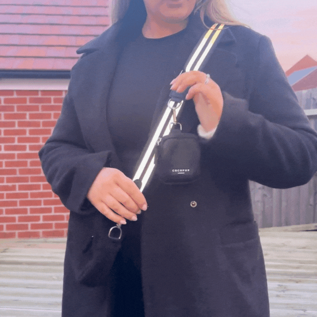 Cocopup London bag with a black reflective strap featuring striped detailing, held by a woman in a black coat outdoors.