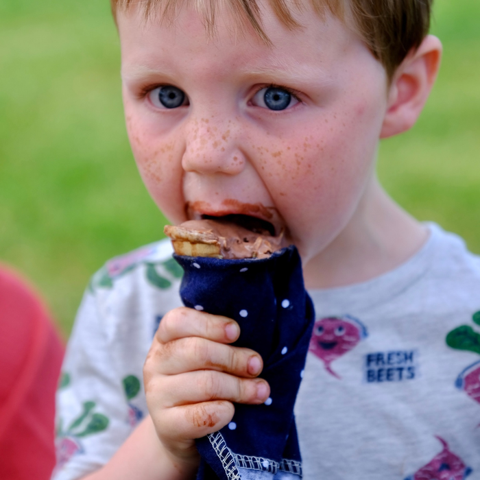 Child eating a chocolate ice cream cone with a polka dot Non-Paper Towel to catch the drips.
