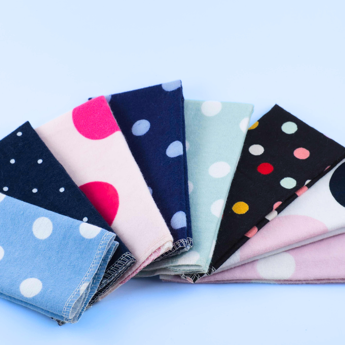 Collection of folded Non-Paper Towels with polka dot patterns on a light blue background