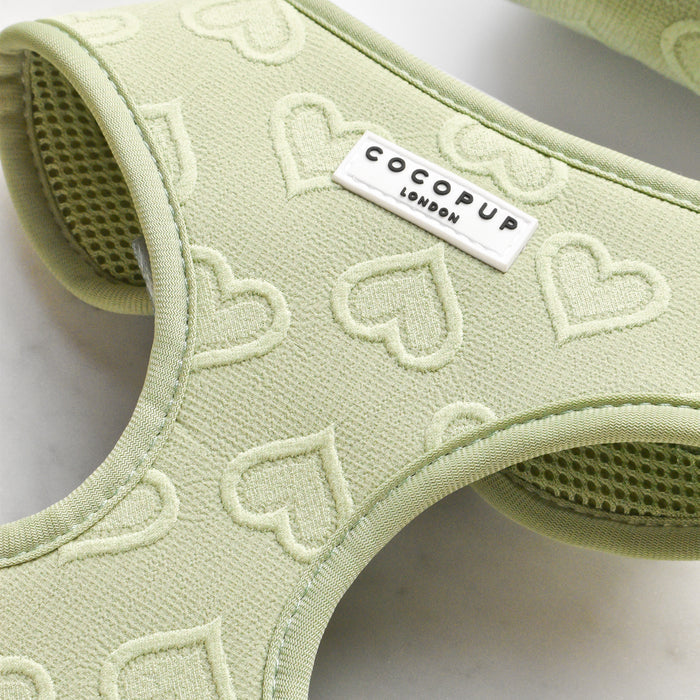 Close-up of the Luxe Adjustable Neck Harness in sage with an embossed heart pattern. This dog accessory features a white label with the brand name "Cocopup London" printed in black letters.
