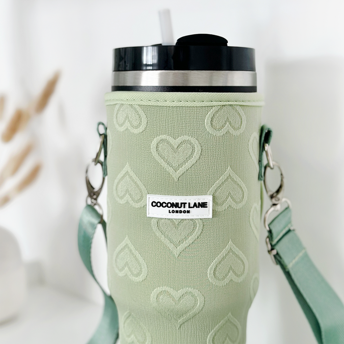 Green tumbler carry case with heart pattern, black lid, straw, and matching cross-body strap.