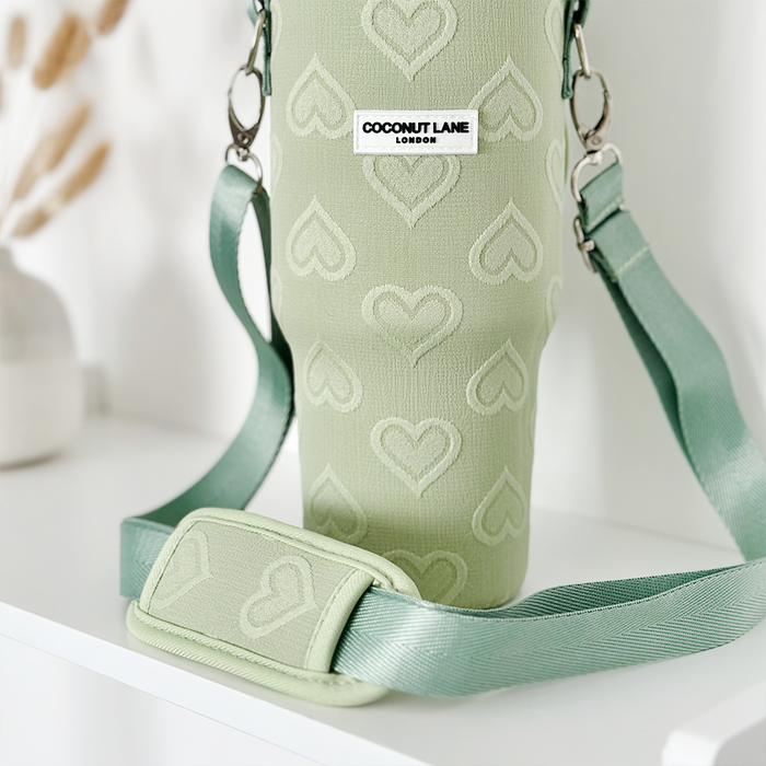 Sage green tumbler carry case with heart pattern and adjustable strap by Cocopup London on a white shelf.