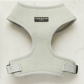 A light gray herringbone Sage Tweed Adjustable Neck Harness from Cocopup London is displayed on a white marble surface. This stylish dog harness features a black label with the brand name "Cocopup London" on the front, and is designed for both comfort and style with its fully adjustable straps and plastic buckles.